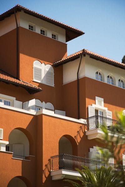 Terracotta-colored Mediterranean-style building with arched balconies and white shutters, set against a clear blue sky