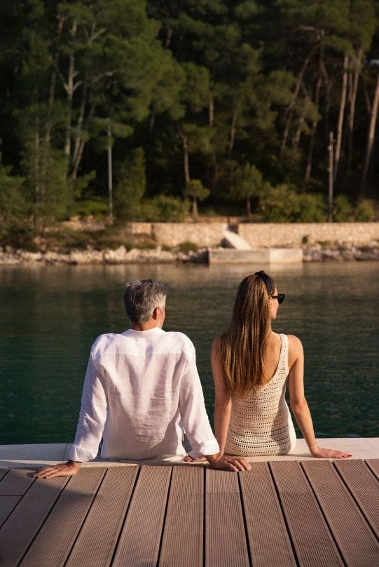 A couple sitting by the water's edge, looking out at a peaceful forest across the bay