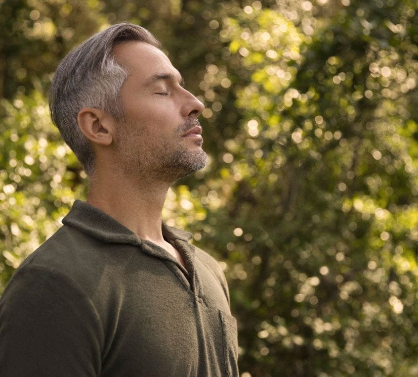 Man with eyes closed enjoying the peace of a sunlit forest, immersed in a moment of tranquility