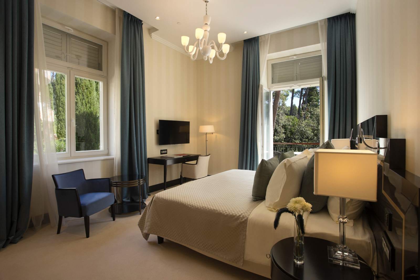 An elegantly appointed room with large windows, draped in translucent curtains, offering a view of verdant greenery