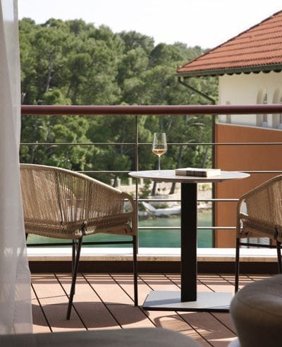 A cozy balcony setup with a table and chairs overlooking the lush surroundings and a hint of the sea