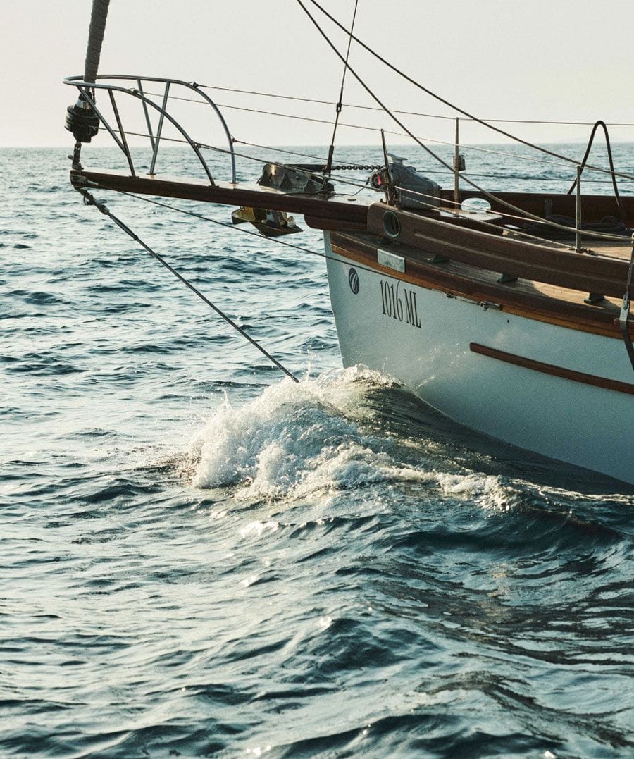 Bow of a sailing yacht cutting through blue waters, with the boat's number visible on the side